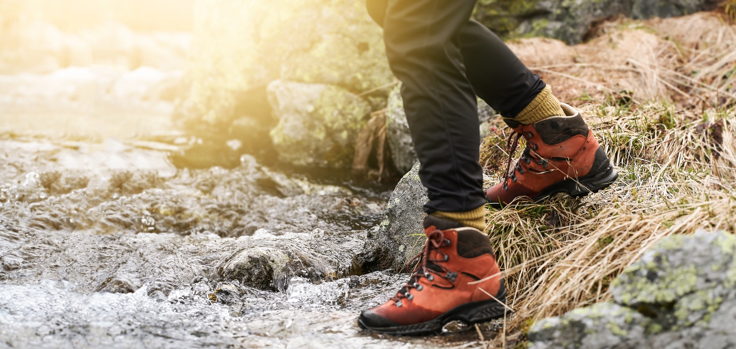 person wearing hiking boots stepping into mountain stream