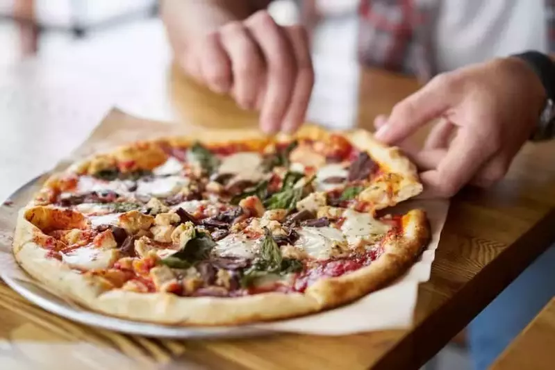 A man pulling a slice from a delicious pizza.