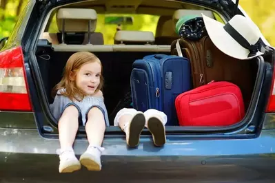 Little kids in the back of a van with suitcases.