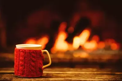 A mug with a wool koozie on a table in front of the fireplace.