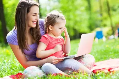 Mother and daughter using laptop in the grass outside of their Murphy NC cabin with internet access.