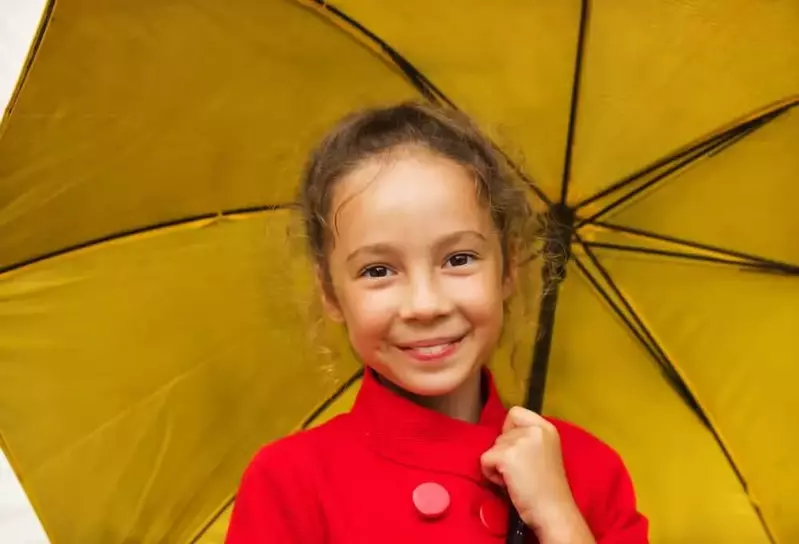 Little girl smiling with an umbrella on a rainy day